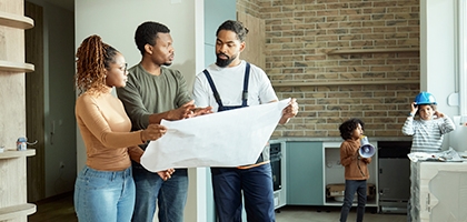 Couple looking at blueprints with contractor while kids play.