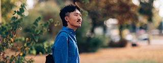 A man in a blue shirt holding a coffee cup while standing outdoors in a park setting.
