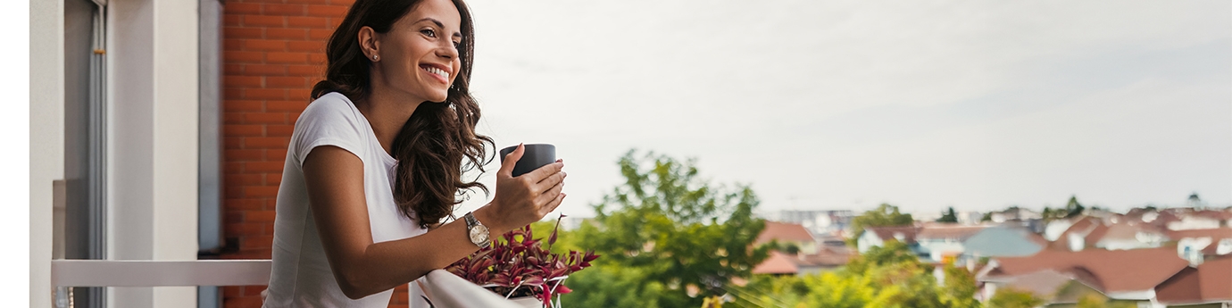 Young woman smiling while holding a coffee cup on a balcony.