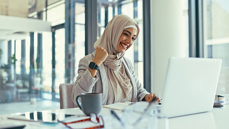 A woman celebrating while using a laptop.