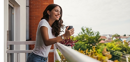 Young woman smiling while holding a coffee cup on a balcony.