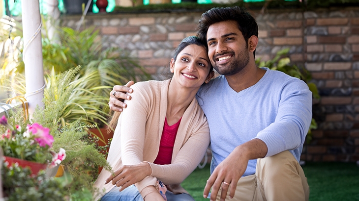 Happy couple sitting on porch by plants.